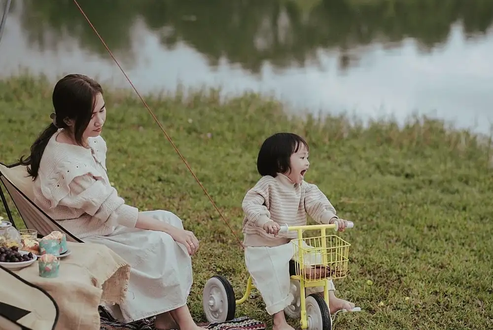 芝生でくつろぐ女性と、黄色い三輪車に乗った子ども